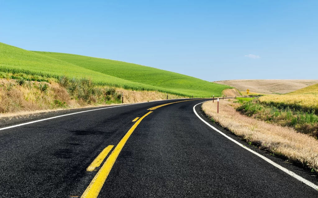 Curved Road Green Hills Blue Sky Yellow Lines