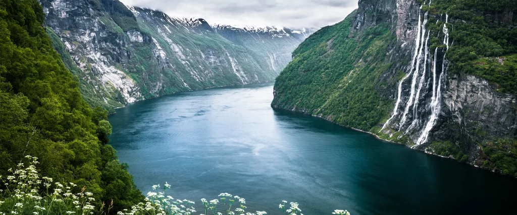 Narrow fjord, steep cliffs, lush greenery, waterfalls, serene, misty