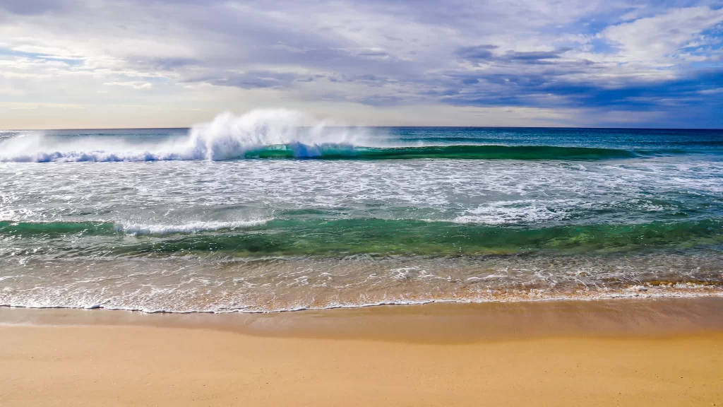 Ocean waves sandy beach blue sky white clouds sunlight sea foam