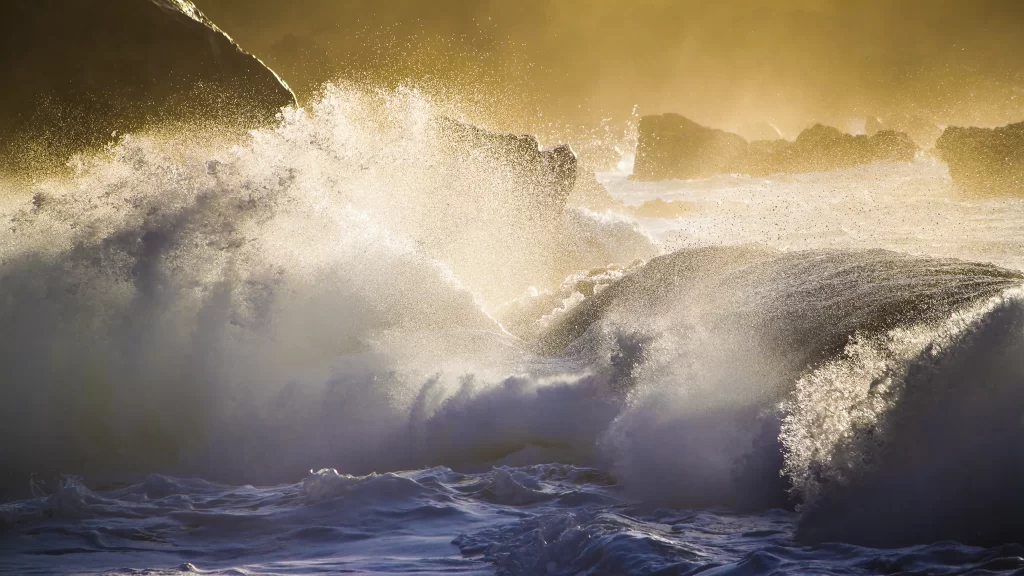 Ocean waves sunlight splashing rocky shore golden glow dynamic water natural bea