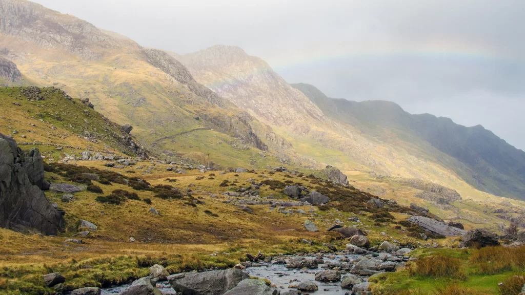 Rainbow mountains stream rocks grass mist sunlight landscape