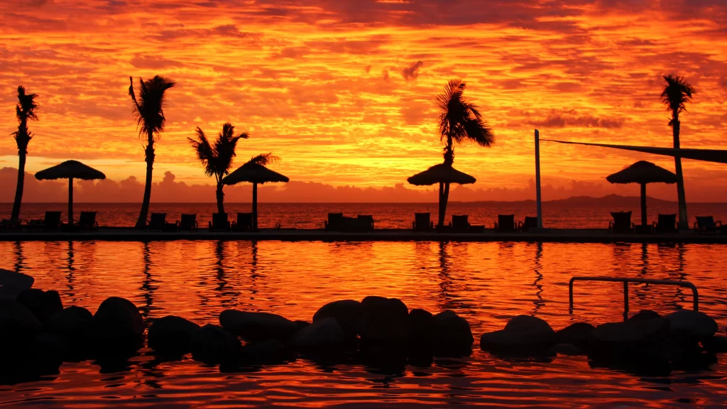 Sunset beach palm trees umbrellas pool sky
