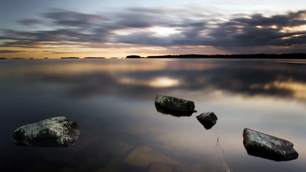Sunset calm water rocks reflection clouds horizon