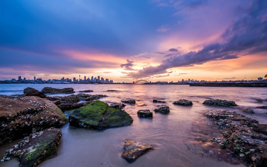 Sunset cityscape skyline water rocks clouds reflection tranquil