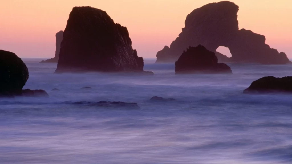 Sunset ocean rock formations waves sky silhouette