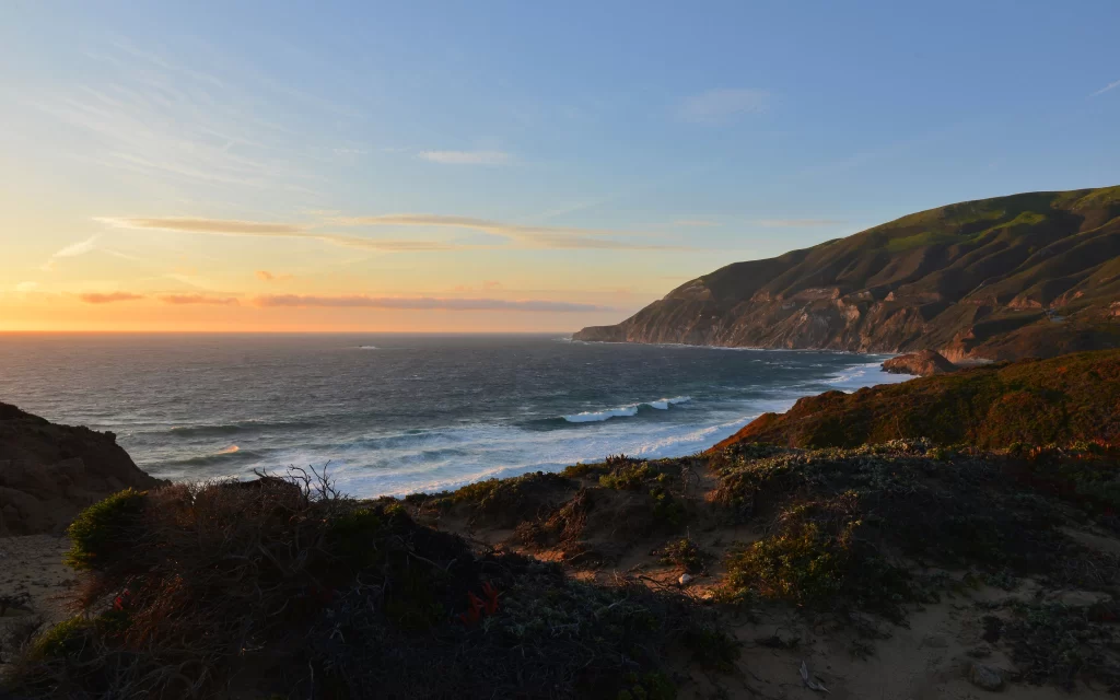 Sunset ocean waves coastline cliffs vegetation sky clouds