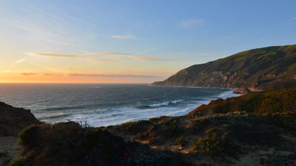Sunset ocean waves coastline cliffs vegetation sky clouds