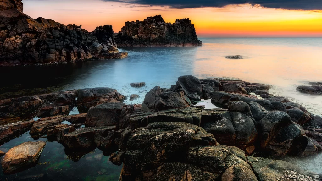 Sunset rocky shore calm sea orange sky tranquil natural beauty