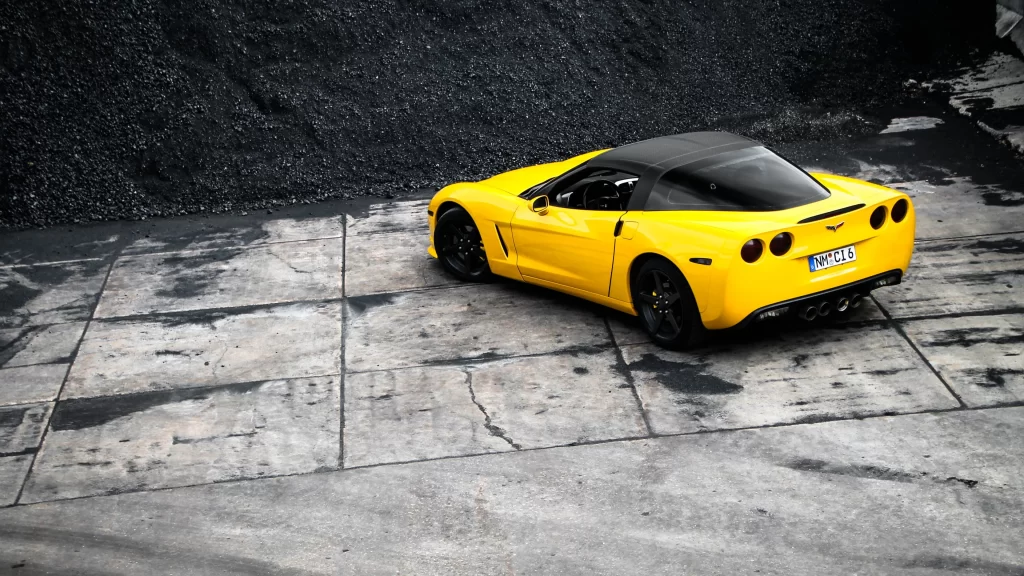 Yellow car black roof sports car license plate concrete surface gravel parking a