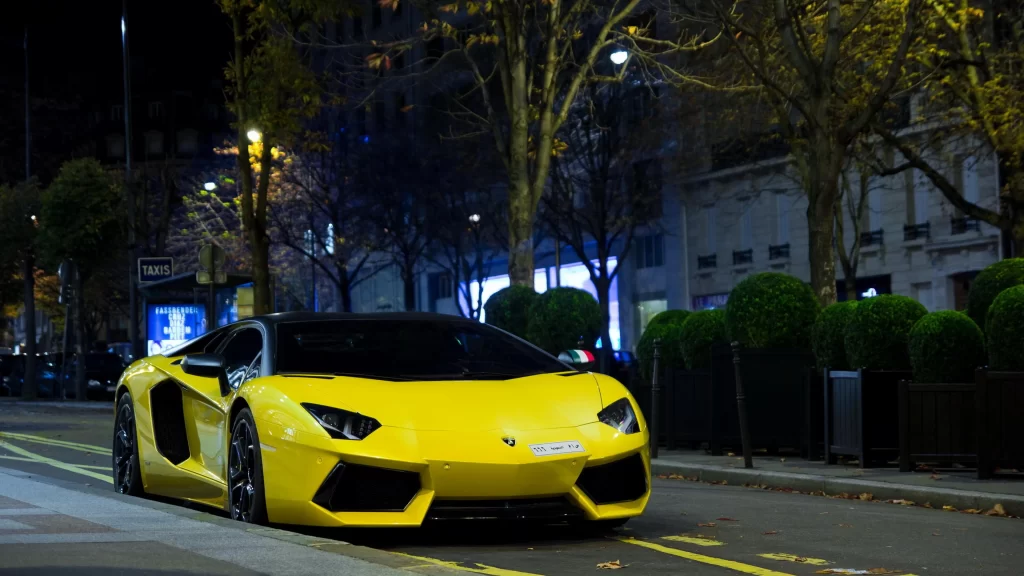 Yellow sports car city street night trees buildings streetlights