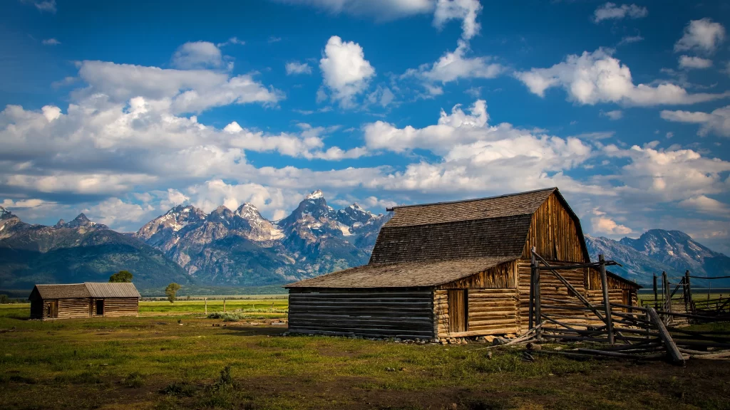 barn mountains sky clouds grass fence