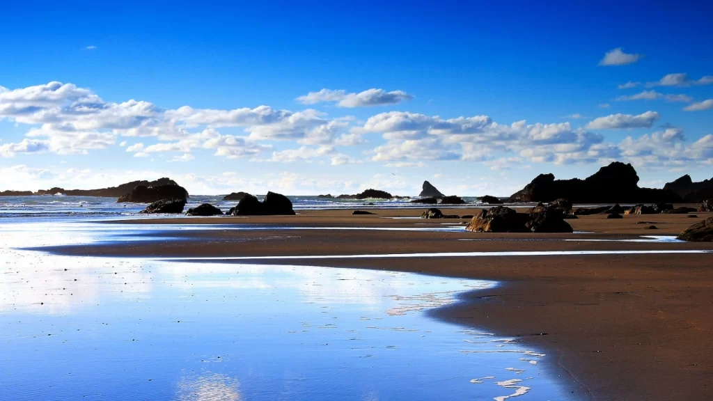 beach ocean rocks sky clouds reflection