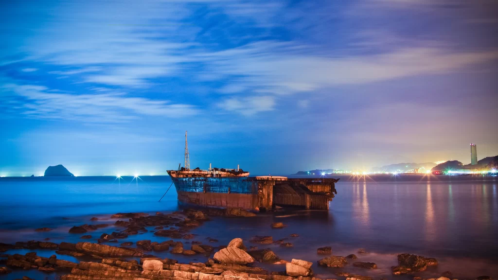 boat water sky clouds rocks night lights city