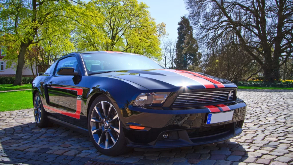 car black red stripe cobblestone trees sunlight