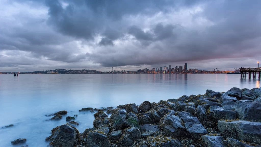 cloudy sky cityscape calm water rocky shore urban lights