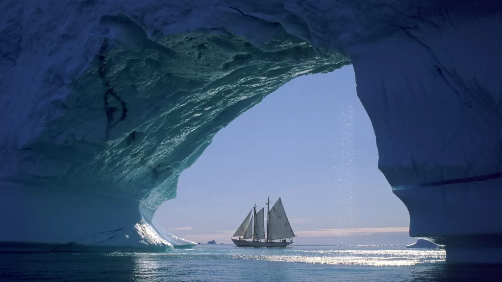 iceberg sailboat ocean water sunlight reflection