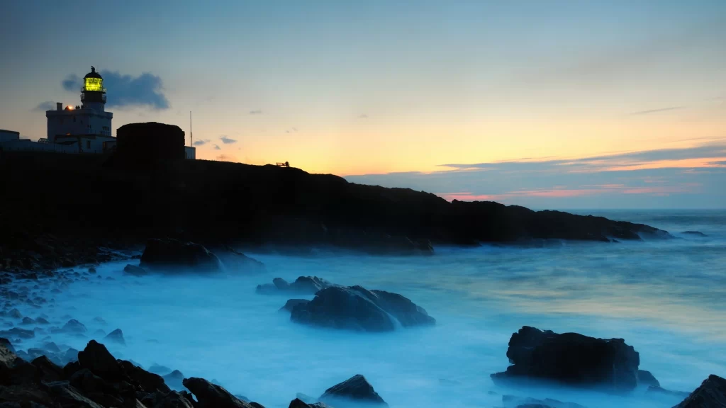 lighthouse sunset ocean rocks waves sky