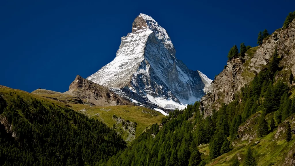 mountain snow peak clear sky green trees rocky terrain