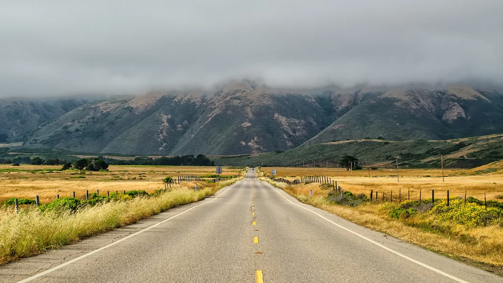 road mountains clouds grass fence landscape