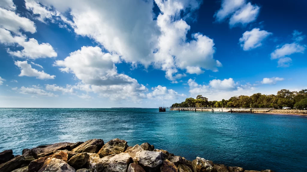 sky clouds sea rocks pier trees