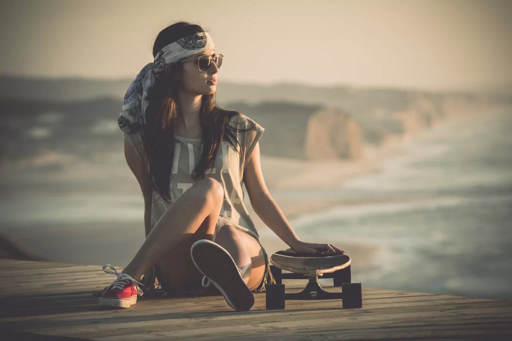 young woman skateboard beach sunset casual sunglasses