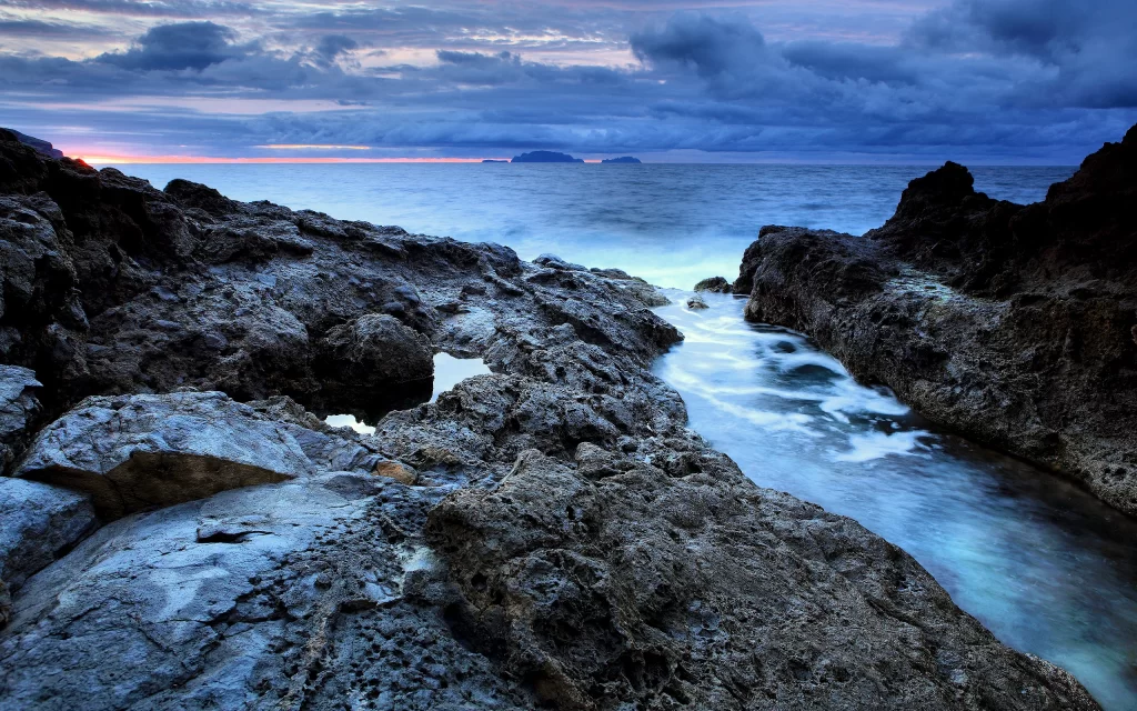 Rugged Coastline Ocean Waves Rocky Shore Cloudy Sky Sunset Blue Tones